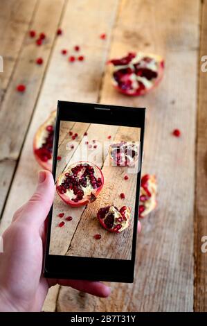 Food Photography on Mobile Phone. Woman Makes Photo Pomegranate on Smartphone. Stock Photo