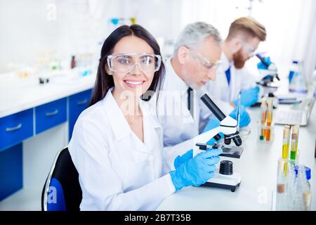 Success in inventing new technology! Young lab worker is smiling and her colleagues are working for experiment. They have all modern equipment they Stock Photo