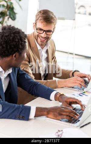 two multiethnic businessmen using laptops at table in office Stock Photo