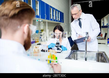 Teamwork and teambuilding concept. A group of three scientists in labcoats are working for new invent Stock Photo