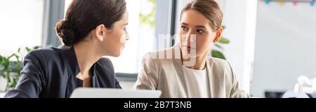 panoramic shot of two businesswomen in formal wear talking in office Stock Photo