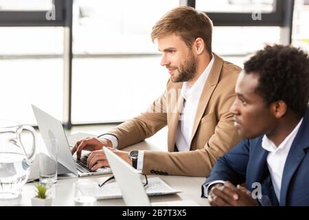 two multiethnic businessmen using laptops at table in office Stock Photo