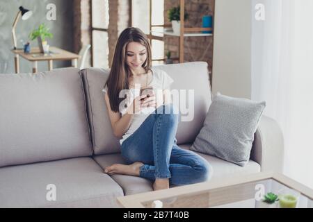 Pretty young woman sitting on couch at home and typing sms to her boyfriend Stock Photo