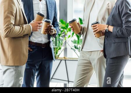 cropped view of four multiethnic businesspeople holding disposable cups of coffee in office Stock Photo