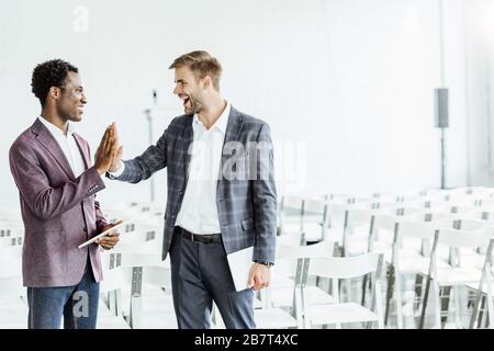 two multiethnic colleagues in formal wear holding digital tablets in conference hall Stock Photo