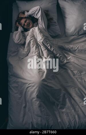 top view of paranormal girl in nightgown with headache lying in bed Stock Photo