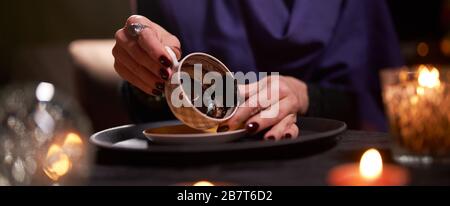 Woman fortune teller divines on coffee grounds at table with ball of predictions in room Stock Photo