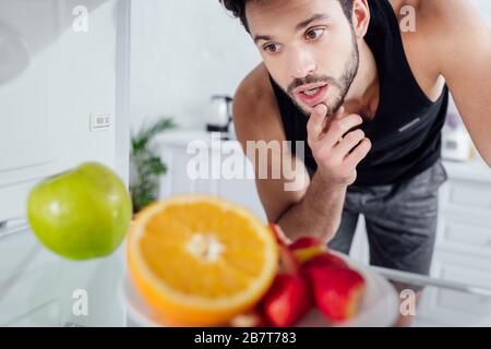 selective focus of pensive man looking at fruits in fridge Stock Photo