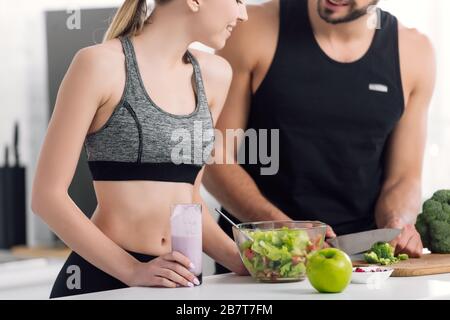 cropped view of cheerful woman holding glass of smoothie near man cooking in kitchen Stock Photo