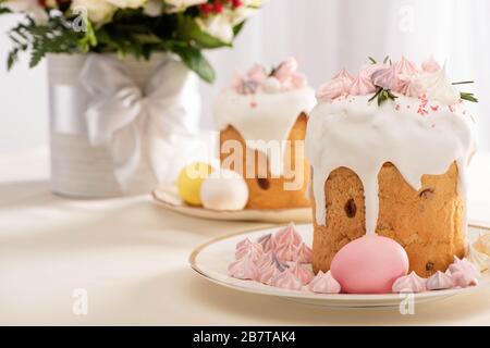 selective focus of festive Easter cake decorated with meringue near painted eggs on plates and flowers Stock Photo