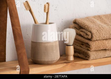 Close up view of shelf with toothbrush holder with toothbrushes, towels and shaving brush in bathroom, zero waste concept Stock Photo