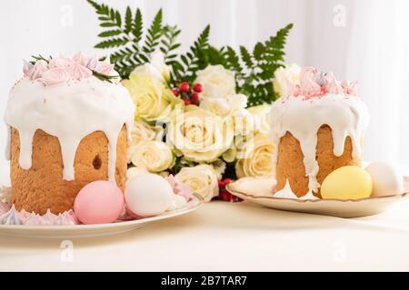 delicious Easter cakes decorated with meringue with colorful eggs on plate near flowers Stock Photo