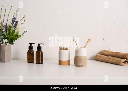 Flowerpot, eco body cream, toothbrush holders with hygiene objects and towels in bathroom, zero waste concept Stock Photo
