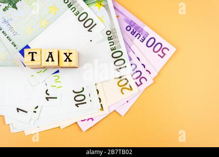 the word tax and the currency of the European Union of different denominations on an orange background 4 Stock Photo