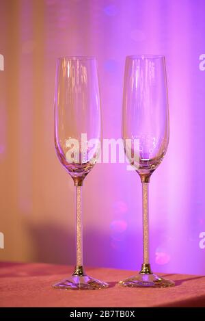 Two empty elegant champagne flutes on a table under artificial purple light, usual recipients for a toast, a welcome, a greeting, a wedding reception Stock Photo