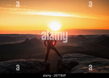 Man hiking silhouette in mountains, sunset jumping. Male hiker with walking sticks on top of mountain risk Stock Photo