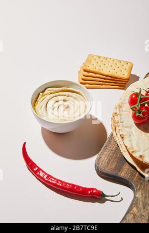 Bowl with delicious hummus, bread and tomatoes on wooden background ...