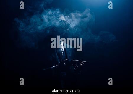 Silhouette of gangster holding gun and smoking on dark background Stock Photo