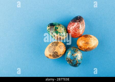 Five easter eggs painted in blue, green, red and yellow lie in a circle. Painted easter eggs on a blue background. Flat lay. Copy space. Stock Photo