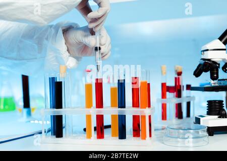 cropped view of scientist holding syringe near test tubes with samples Stock Photo