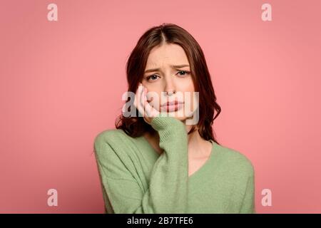 upset girl looking at camera while touching face isolated on pink Stock Photo