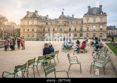 Paris France, 23 February 2020 : People resting on iconic green chairs at Jardin du Luxembourg gardens in front of the French Senate building in Paris Stock Photo