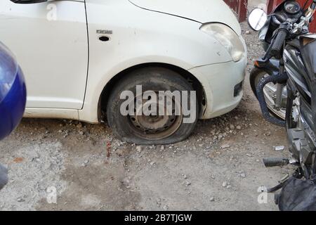 Tire leak, close up wheel of old white vintage car. Car wheel flat tire on the road. Deflated tyre of an old car next to a motorcycle parked long time Stock Photo