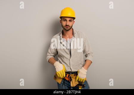 confident worker in helmet and gloves with tool belt on grey Stock Photo