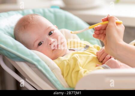 Mom feeds baby vegetable puree in a high chair. The toddler refuses to eat. The infant doesn't want to nutrition. The kid turned away from the food sp Stock Photo