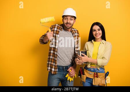 emotional manual workers with paint roller and paint can on yellow Stock Photo