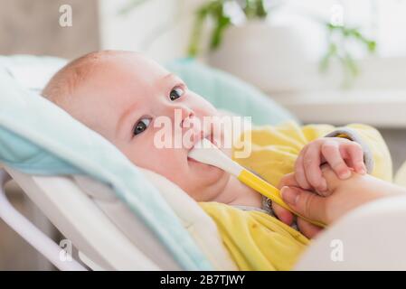 Mom feeds baby vegetable puree in a high chair. The mother puts a spoon of mashed in the child's mouth. The infant eats food. Stock Photo