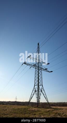 High voltage transmission tower on a field against the sun. Stock Photo