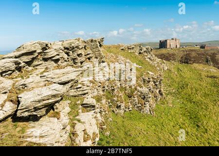 Rocky landscape on the island of Tintagel Castle, with the 'Camelot Castle Hotel' (1899) on the distant headland.  Tintagel, Cornwall, UK. Stock Photo