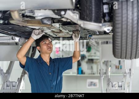 Asian mechanic repairing and light up under the car in maintainance service center which is a part of showroom, technician or engineer professional wo Stock Photo