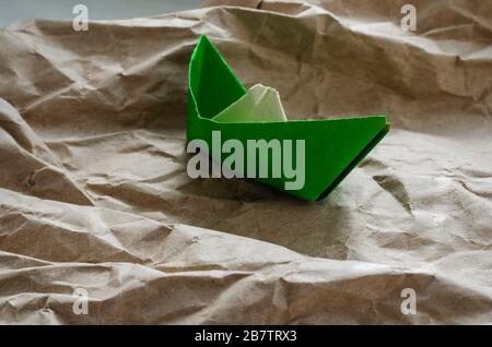 Old paper boat on paper waves. Origami from jammed and torn green paper. Goal Achievement Concept. Eye level shooting. Side view. Selective focus. Stock Photo