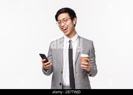 Office workers, business and lifestyle concept. Waist-up portrait of lucky cheerful asian male entrepreneur calling friend using wireless earphones Stock Photo