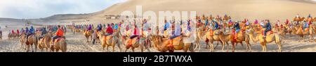 Dunhuang, Gansu, China - September 12, 2018 : Panorama of tourists at camel rides at Singing Sand Mountain dunes of Taklamakan Desert, Dunhuang, China Stock Photo