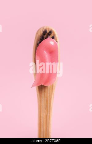 Wooden toothbrush with pink paste close-up on a pink background. Stock Photo