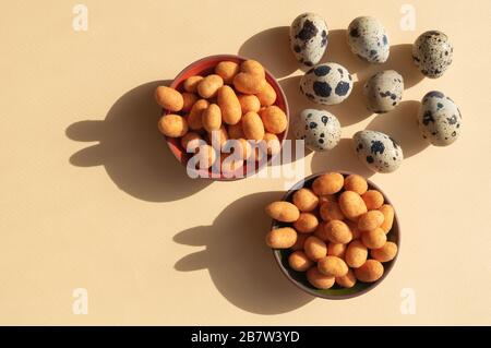Seven quail eggs and two bowls with nuts with shadows like rabbits on the light yellow background. Trendy conceptual minimalistic photo for Easter Hol Stock Photo