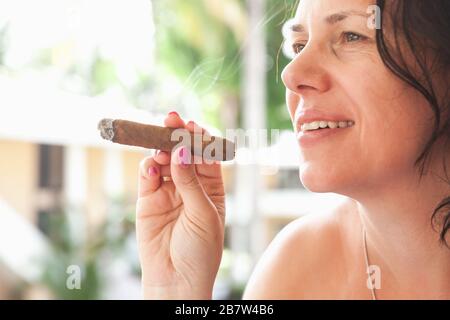 Young smiling woman smokes handmade cigar, close-up outdoor photo with selective focus. Dominican Republic Stock Photo