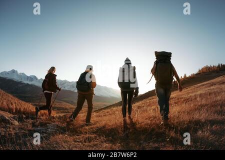 Four unrecognizable hikers or backpackers walks with backpacks in sunset mountains. Trekking in mountains concept Stock Photo