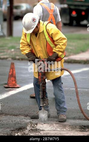 Austin Texas USA: City of Austin construction worker wearing hard hat, protective gloves, thick-soles work boots and an orange safety vest  uses jack hammer to break up asphalt on roadway. ©Bob Daemmrich Stock Photo