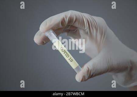 Hand in medical glove with a lab container - 'covid 19' on it. vaccination, virus research or treatment development concept Stock Photo