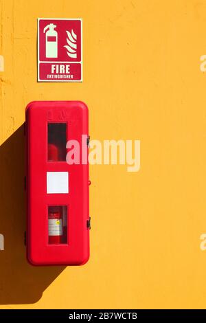 Red fire extinguisher on an outdoor yellow wall for prevention Stock Photo