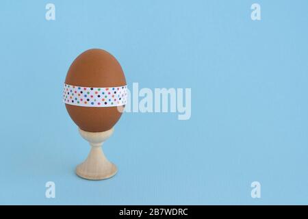 Egg standing on cup, on a soft blue background. Easter egg tied with a festive ribbon Stock Photo