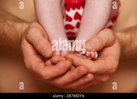 Feet of a newborn baby in the hands of parent. Happy Family concept. Dad hug his baby's legs Stock Photo