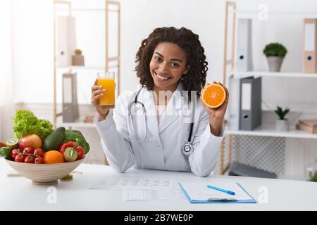 Cheerful female nutritionist holding fresh orange juice Stock Photo