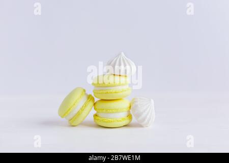 Yellow french macarons and white marshmallows on a white wooden background. Place for text. Stock Photo