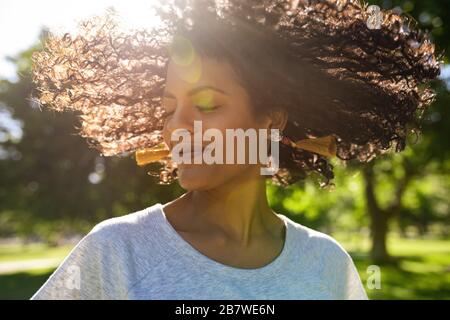 Smiling woman twirling her curly hair outside in a park Stock Photo