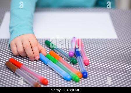 Close-up of five year old boy picking up a light blue pen from a table with white dots. The boy is dressed in a turquoise shirt. Stock Photo